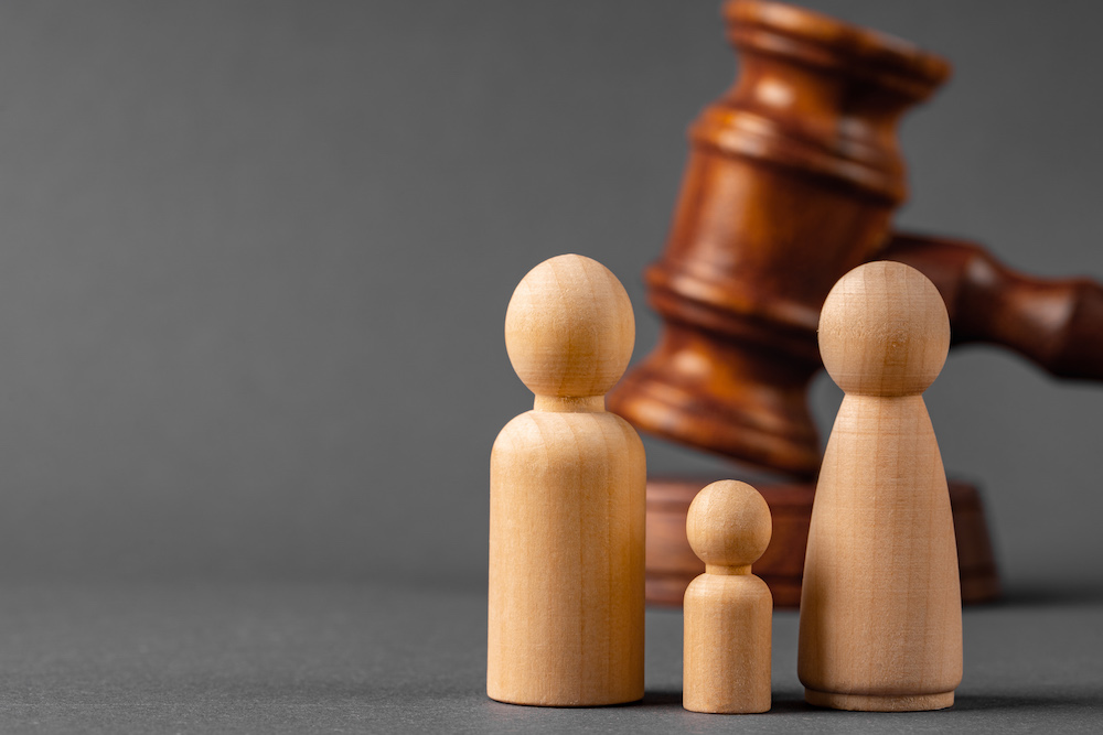Wooden toy family with judges gavel in the background symbolizing a couple separating and going through a custody battle.