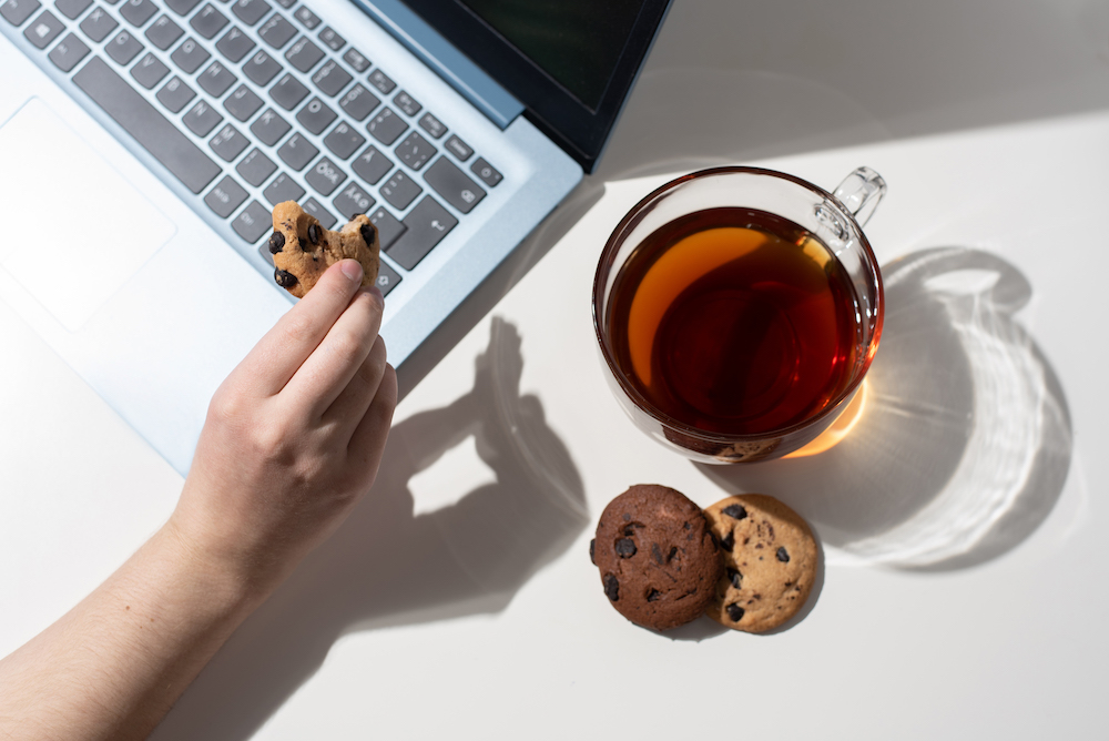 A hand holding a cookie with a computer in the background.