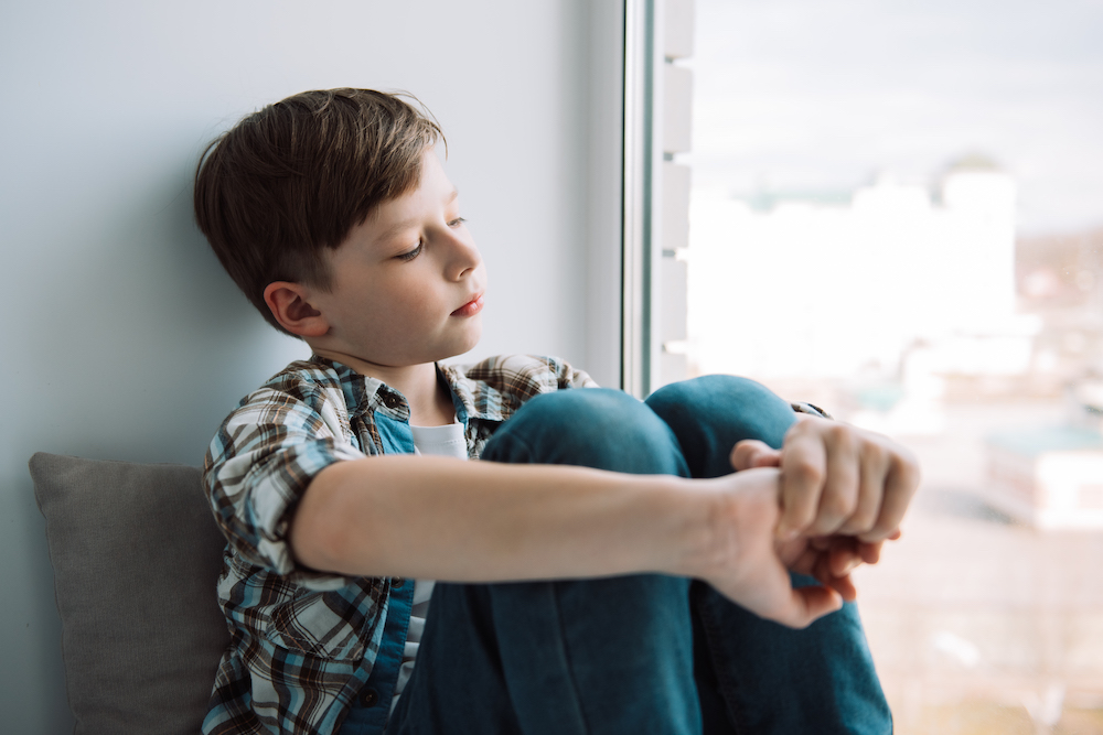 A boy, siting by a window looking out.