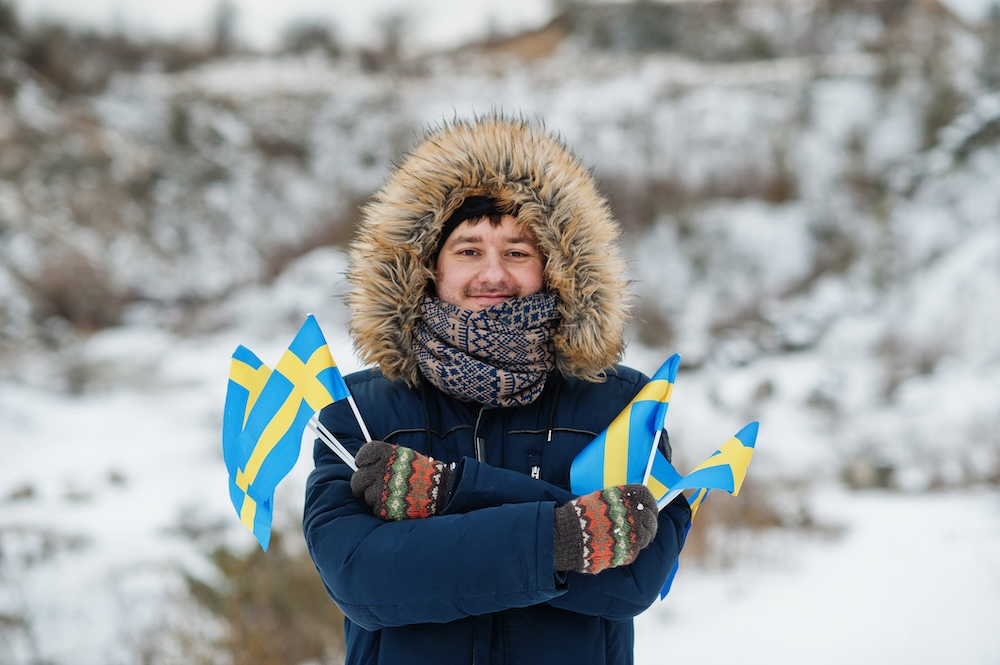 Svensk medborgare. Man ute i vinterlandskap med svenska flaggor i handen.