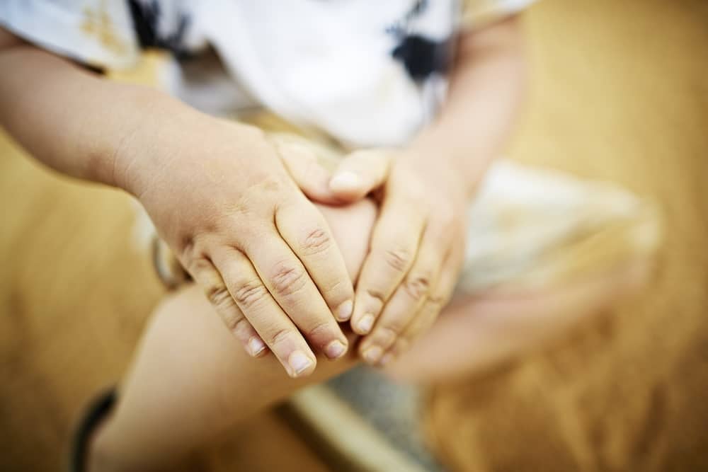 Closeup of childs hands over their knee in article about report concern for a child's welfare