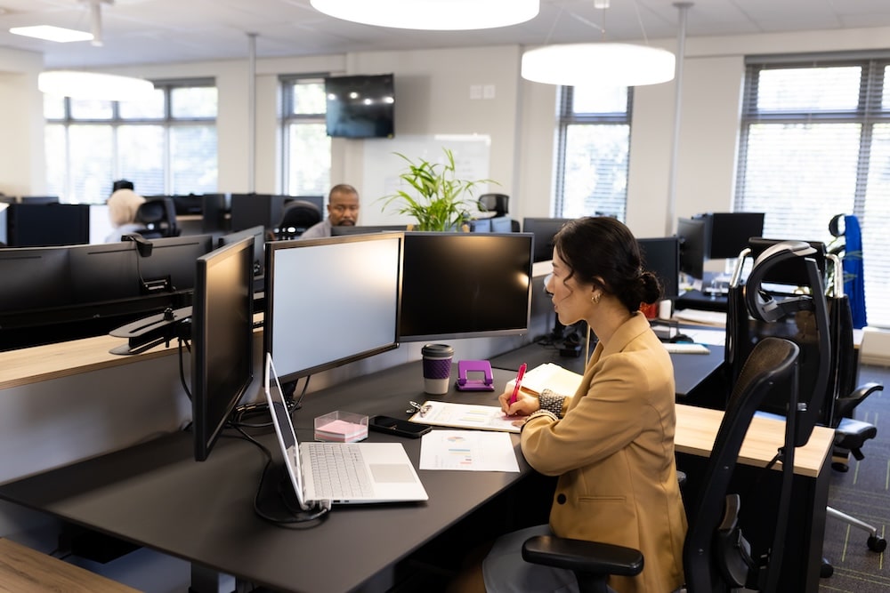 Asiatisk kvinna som sitter vid ett skrivbord på kontor och jobbar vid dator.